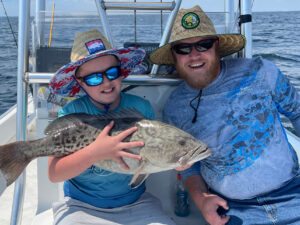 young boy and dad holding a black drum fish aboard a fishing boat in destin florida