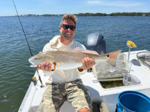 man in white longsleeve sun shirt holding a reddrum fish on a destin inshore fishing boat